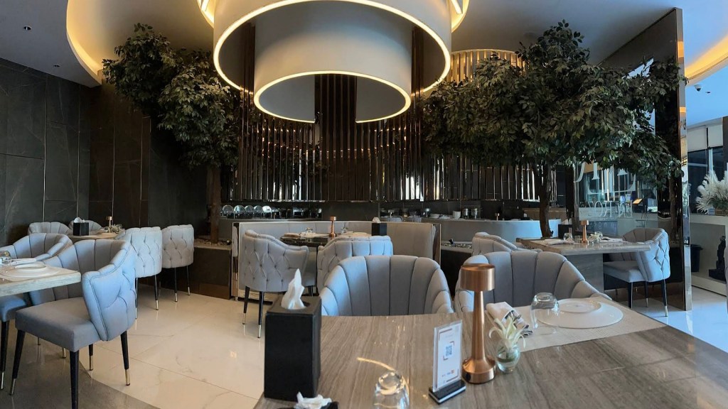 Modern restaurant interior featuring plush chairs, elegant tables, and decorative trees, creating a sophisticated dining atmosphere.