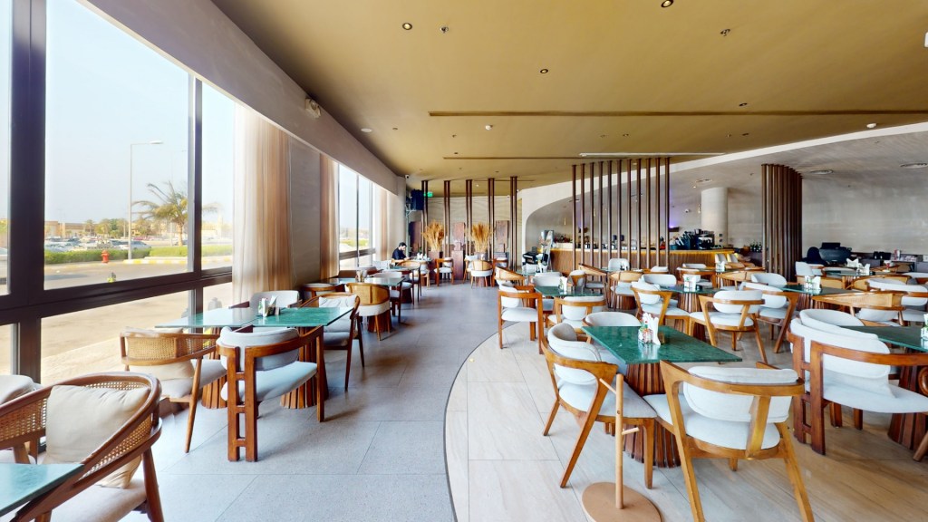 Interior view of a modern restaurant featuring wooden furniture, green tables, and large windows with natural light.
