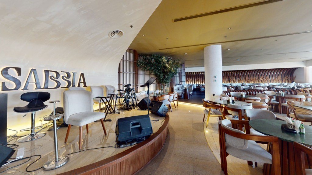 Interior view of a modern restaurant named 'SABIA', featuring a stage with musical instruments, stylish seating, and elegant decor.