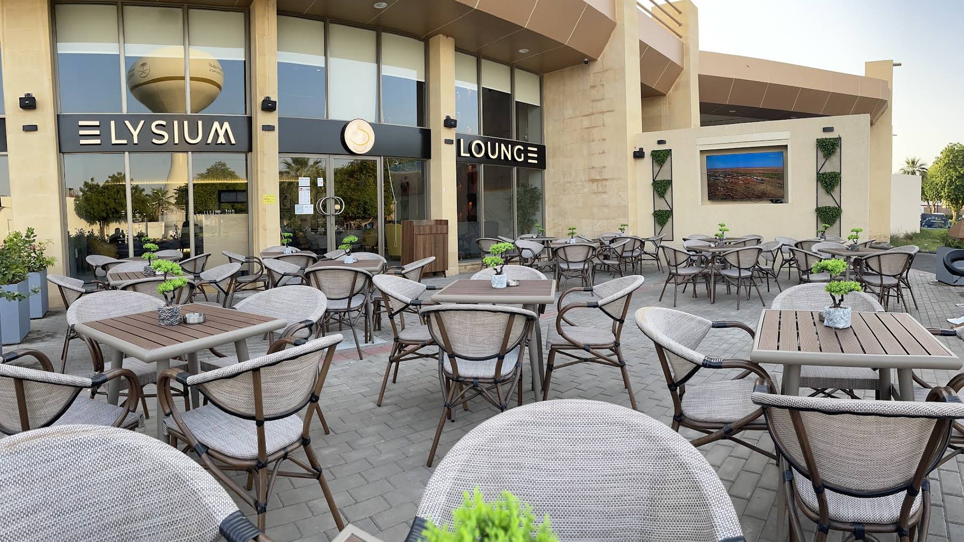 Outdoor seating area of Elysium Lounge featuring tables and chairs with small plants on each table.